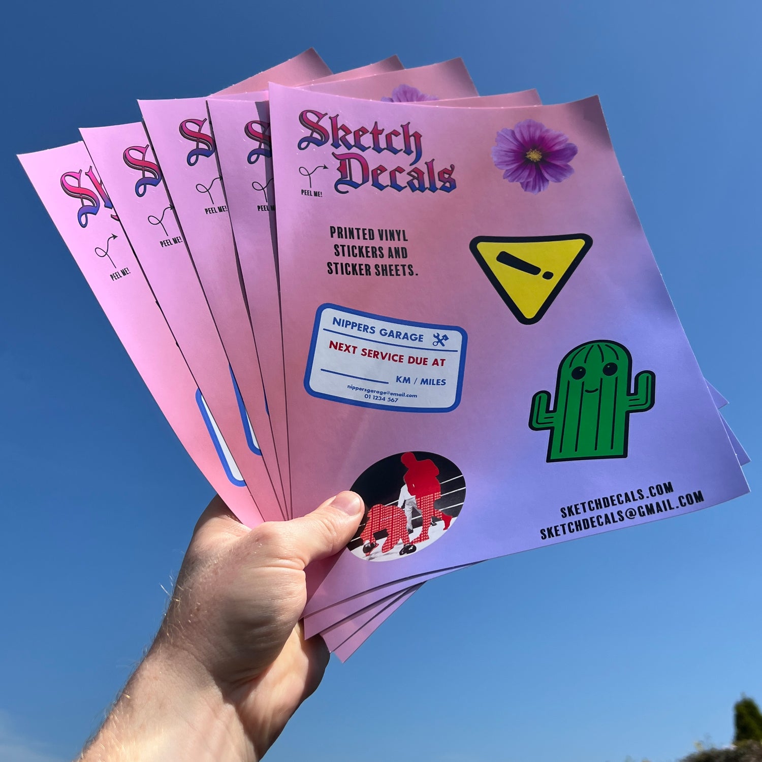 Five sketch decals Custom A4 Vinyl sticker sheets being held in the air